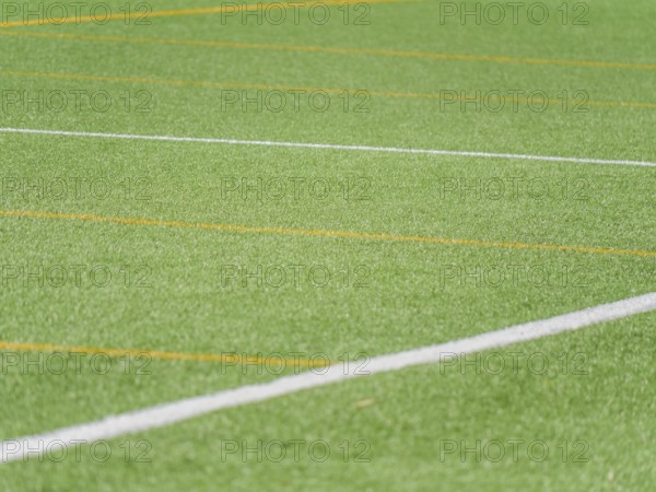 A close up view of a green artificial turf soccer field, featuring vibrant white and yellow lines intersecting diagonally, ideal for backgrounds or soccer related content and its textures