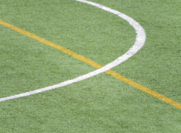 A close up of white and yellow lines marking a soccer field on artificial green turf. The detailed view highlights the texture and precise lines used in field design
