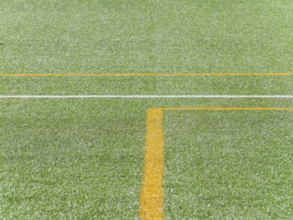A close up view of vibrant green artificial turf with distinct yellow and white lines, creating geometric patterns. The texture offers a realistic, fresh appearance suitable for soccer