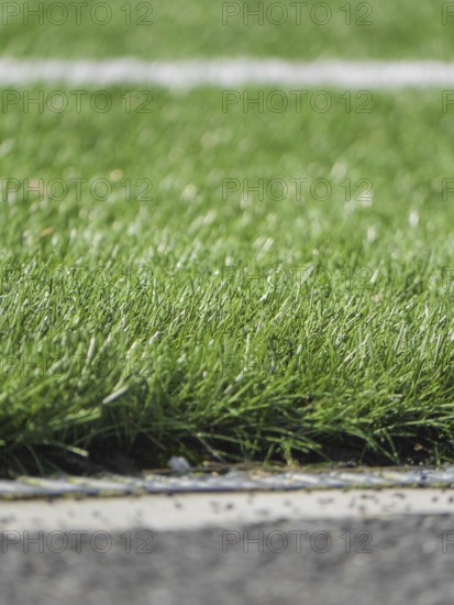 A close up image of vibrant artificial grass with a white line, depicting a section of a synthetic soccer field. The textured surface showcases detailed grass blades