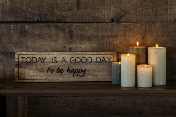 A motivational sign with the words Today is a good day to be happy rests on a rustic wooden shelf, accompanied by glowing candles, creating a cozy and uplifting ambiance