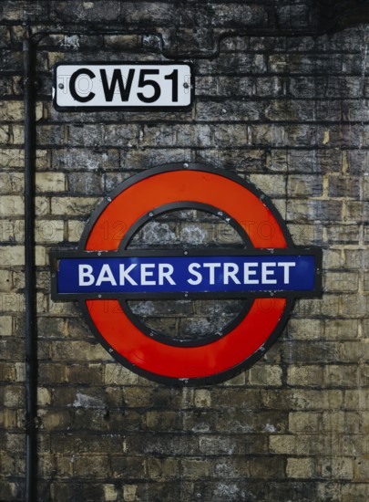 A vibrant image of the Baker Street station sign on London's Underground, set against a textured brick wall. The sign's classic design highlights the station's historical significance