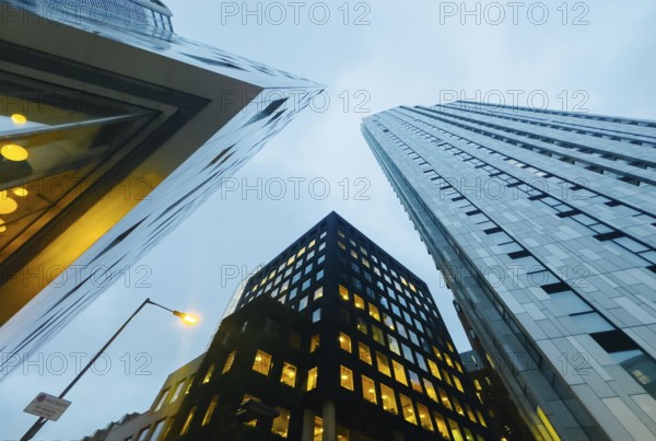 Low-angle view of modern skyscrapers in London at dusk, showcasing their sleek design and illuminated windows. The urban landscape is framed by a cloudy sky, creating a dynamic city scene
