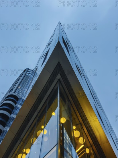 A striking view of a modern glass building in London's skyline, showcasing sharp angles and reflecting the blue sky. Warm lights create a contrasting ambience