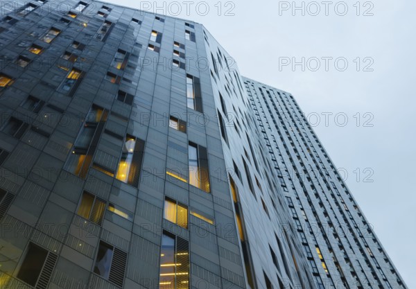 A low-angle view of modern skyscrapers in London, showcasing sleek design and illuminated windows against a cloudy sky, highlighting urban architectural details
