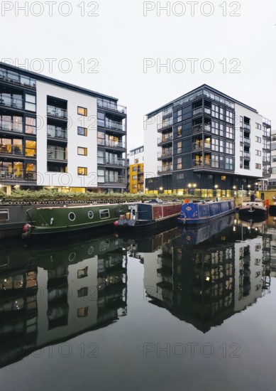 A modern London cityscape features sleek apartment buildings and colorful canal boats reflected in calm water, showcasing a blend of urban living and tranquil waterways