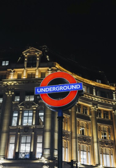 A vibrant shot of the classic London Underground sign glowing against an elegant, illuminated building facade at night, capturing the essence of urban life