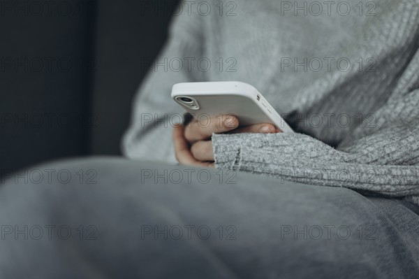 A person in a soft gray sweater holds a smartphone, reflecting a comfortable and relaxed moment. The casual setting emphasizes simplicity and technology