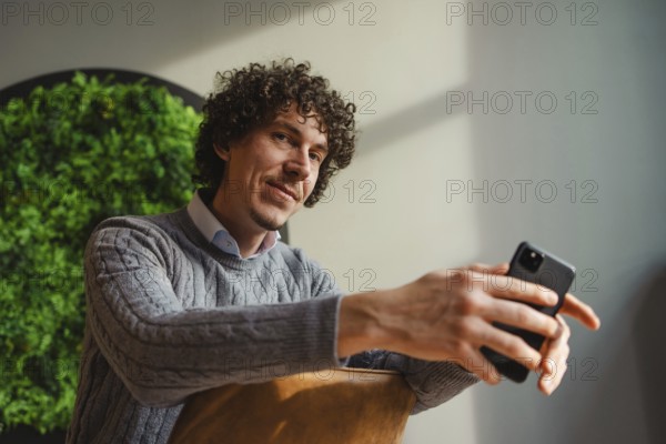 A curly-haired young man, sitting against a vivid green wall, emphasizes themes of ecology and sustainable development. The setting combines modern style with a focus on nature