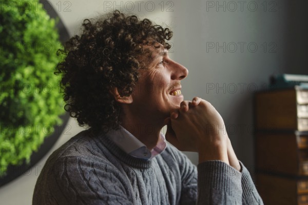 A curly-haired young man smiles contemplatively, sitting against a vibrant green wall. The imagery highlights themes of ecology and sustainable development, emphasizing a connection to nature