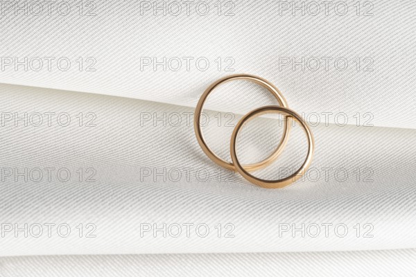 A pair of golden wedding rings overlap on a soft textured fabric, symbolizing love and commitment