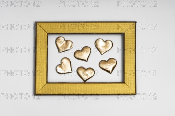 A collection of golden heart shapes arranged inside a textured gold frame, evoking themes of love and romance, perfect for St. Valentine's Day and wedding decorations