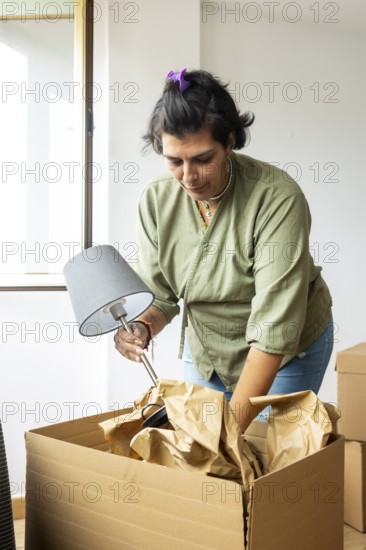 A trans woman is unpacking a lamp from a cardboard box in her new home, symbolizing fresh starts and personal growth. The scene exudes confidence and pride in her identity