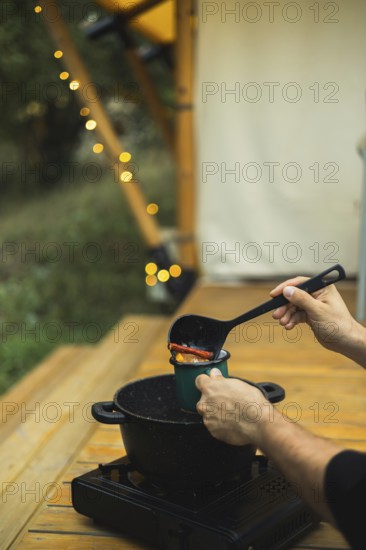 Cropped unrecognizable person pours spicy mulled wine into a mug, outdoors near twinkling lights
