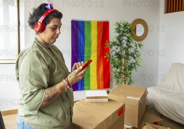 A transgender woman joyfully explores her new home, decorated with a rainbow flag symbolizing LGBTQIA+ pride. She listens to music, surrounded by moving boxes