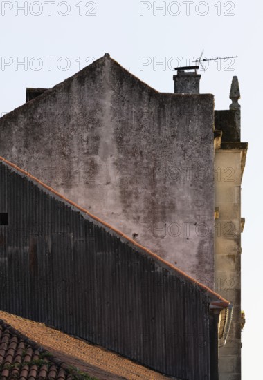 A close-up shot of aging, rustic rooftops with orange tiles, contrasting with the worn and weathered walls. A distant chimney and antenna add to the vintage, nostalgic atmosphere