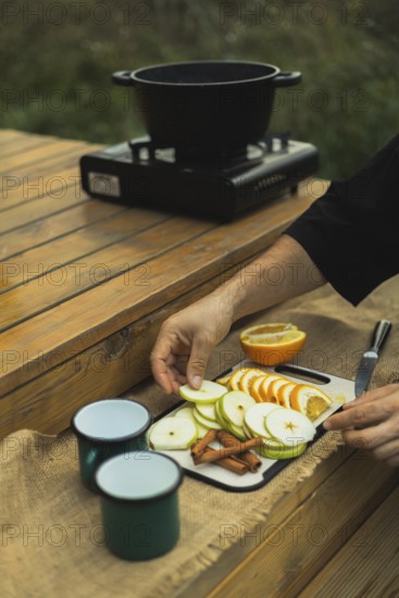 Cropped unrecognizable man slices fruits on a wooden table for mulled wine, outdoors