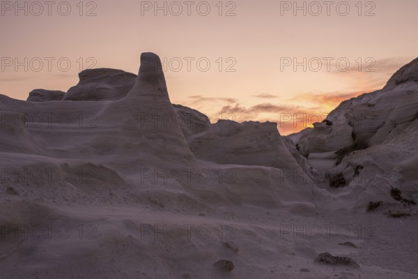 Dramatic sunset casting a warm glow over the sculptural white rock formations of Sarakiniko on the island of Milos, Greece