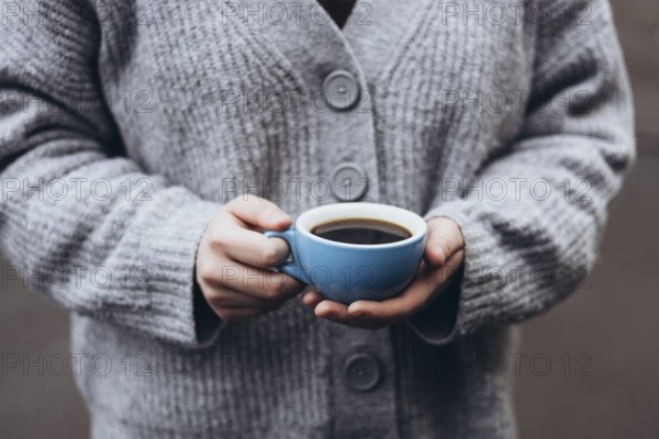 A person in a cozy gray sweater holds a blue cup coffee, capturing a peaceful moment of warmth and comfort, perfect for a chilly day