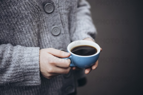 A person in a cozy sweater holds a steaming cup of coffee, providing warmth and comfort on a chilly autumn morning. The soft focus adds to the tranquil atmosphere