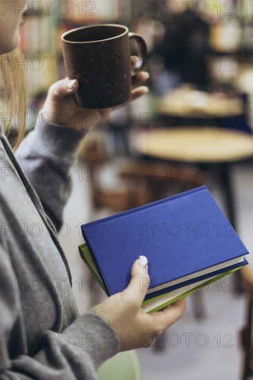 A woman in casual attire holds a coffee mug and books, enjoying a quiet moment in a cozy bookstore setting. Perfect for themes of relaxation, reading, and comfort
