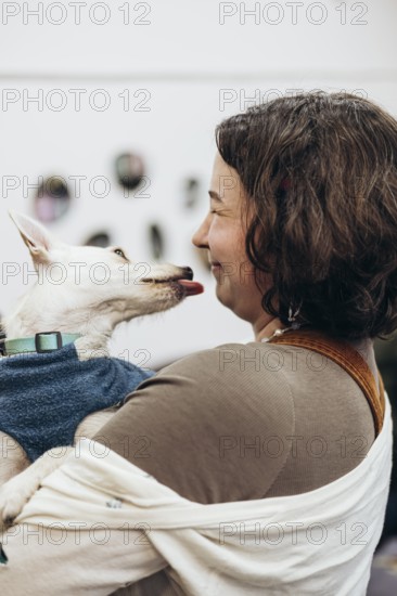 A young woman shares a joyful moment with her dog as it playfully licks her face in a bookstore. Captured in a warm, indoor setting, this image conveys affection and companionship