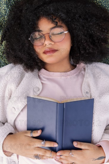 A peaceful latin woman in glasses rests with a book on a cozy day indoors. The scene captures relaxation, comfort, and the joy of reading, offering a serene moment of leisure