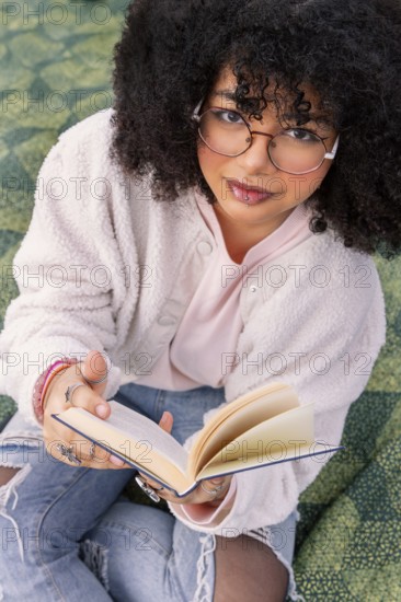 A young latin woman with glasses enjoys reading a book while sitting comfortably. Her casual style and focus create a relaxed, intellectual atmosphere