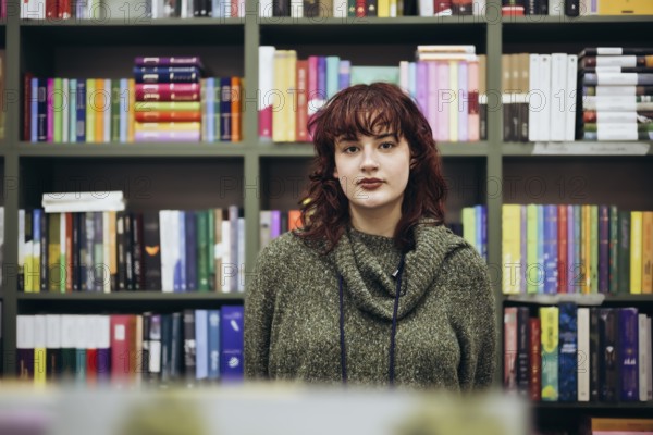 A young woman stands confidently in front of a vibrant, well-stocked bookcase, her expression thoughtful and serene