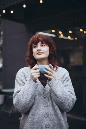 A young woman enjoys a coffee in a cafe terrace, wearing a cozy sweater, surrounded by string lights. The ambiance is tranquil and inviting, perfect for a leisurely coffee break
