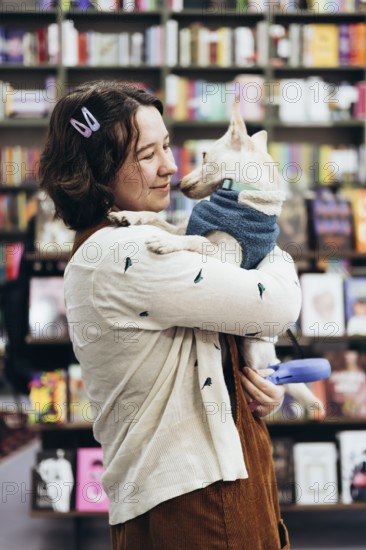 A young woman holds her dog lovingly in a warm bookstore, surrounded by colorful books. The cozy atmosphere and the pet human connection create a heartwarming scene