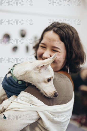 A smiling young woman tenderly holds a dog, capturing a moment of joy and companionship in a bookstore. The neutral backdrop emphasizes the bond between them, highlighting love and care