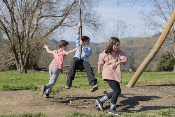 Three friends play joyfully on a zip line in a park, enjoying a sunny day together. Trees and green grass create a vibrant outdoor setting perfect for playful activities