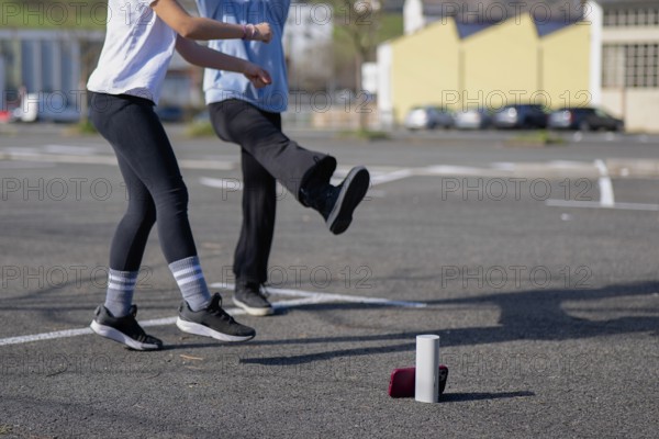 Friends dancing near a speaker and phone in a sunny parking lot. The casual outdoor scene captures a moment of playful exercise and leisure with a tech twist