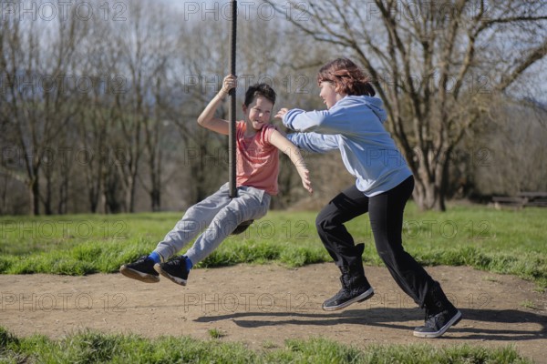 Two friends enjoy a sunny day by playing on a zip line in a park. Laughter and joy fill the air as they take turns pushing each other and swinging high amidst nature