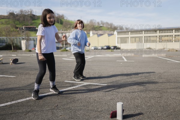 Two friends play a fun game outdoors in an empty parking lot under clear skies. They look engaged and active, highlighting the joy of outdoor play on a sunny day