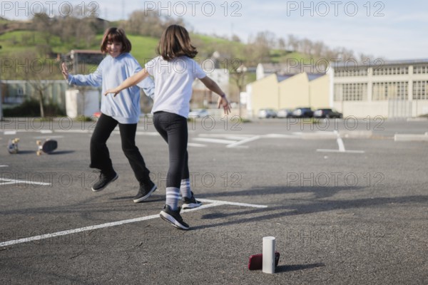 Two friends joyfully dance and play an outdoor game in an empty urban parking lot. Skateboards rest nearby, capturing the essence of an active, carefree day