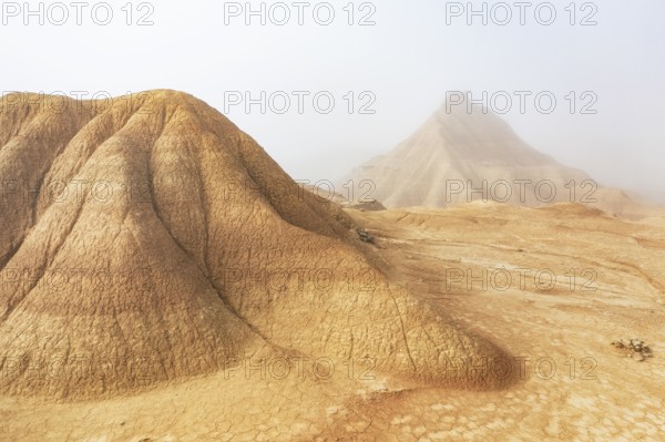 A captivating desert scene with majestic eroded hills shrouded in light mist, creating a mysterious and tranquil atmosphere The pale beige hues enhance the serene ambiance