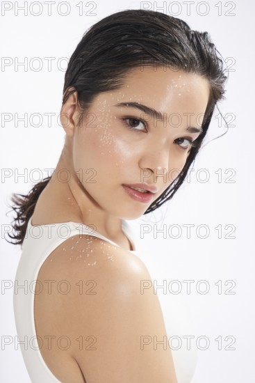 A young woman looks slightly away from the camera in this fresh studio portrait, highlighting her skin adorned with salt crystals