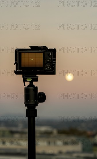 A camera on a tripod silhouetted against a warm sunset sky, overlooking the cityscape of Geneva, Switzerland