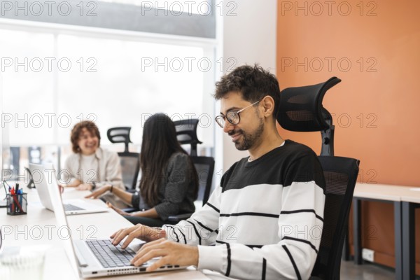 A vibrant office scene displaying coworkers engaged in teamwork, emphasizing collaboration and productivity Colleagues interact and work diligently on laptops