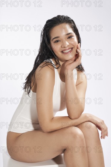 A young female model with a radiant smile and wet hair posing in a studio setting, dressed in a white bodysuit