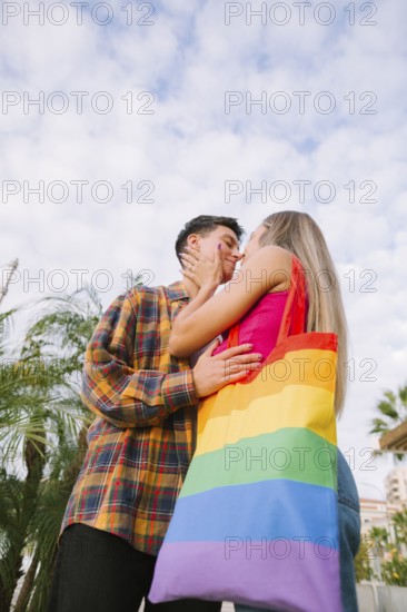 A happy lesbian couple shares a tender moment outdoors, embracing each other's love and connection. A vibrant rainbow tote bag adds a touch of pride and celebration