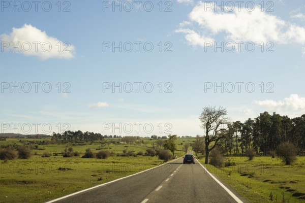 A car travels along a quiet country road under a clear blue sky on a peaceful autumn morning The landscape features lush green fields and scattered trees
