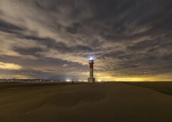 Fangar Lighthouse in Tarragona, Spain stands alone on sandy dunes under a dramatic sky The lighthouse's beacon shines brightly, creating a serene yet dramatic coastal scene