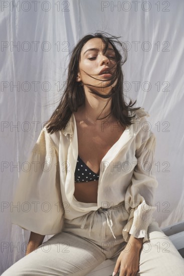 A woman enjoys the summer sun, dressed in a stylish cream blouse and polka dot bikini top The flowing fabric and gentle breeze capture a serene, carefree vibe