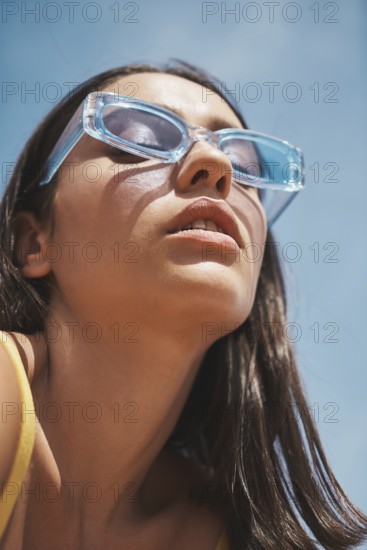A fashionable woman sporting trendy, clear blue sunglasses basks under the vibrant summer sky Her relaxed expression captures the essence of carefree rooftop living