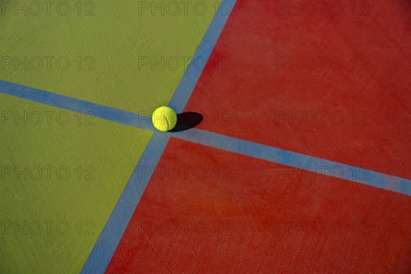 Close-up view of a yellow tennis ball at the intersection of colorful court lines, showcasing the vibrant red and green surface textures