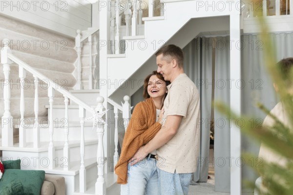 A joyful couple shares a loving embrace inside a well-decorated home, conveying warmth and happiness. The woman, beaming with a wide smile and the man, expressing gentle affection