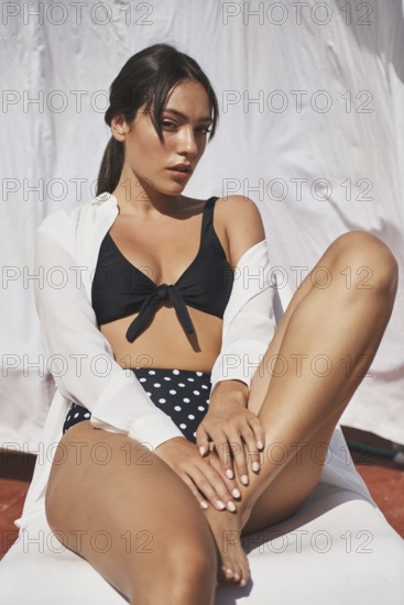 A woman enjoys the summer sunshine on a rooftop, wearing a black and polka-dot swimsuit The scene captures relaxation, fashion, and warmth in a contemporary outdoor setting